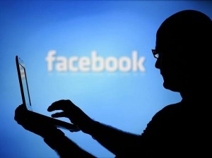 A man is silhouetted against a video screen with an Facebook logo as he poses with an Dell laptop in this photo illustration taken in the central Bosnian town of Zenica